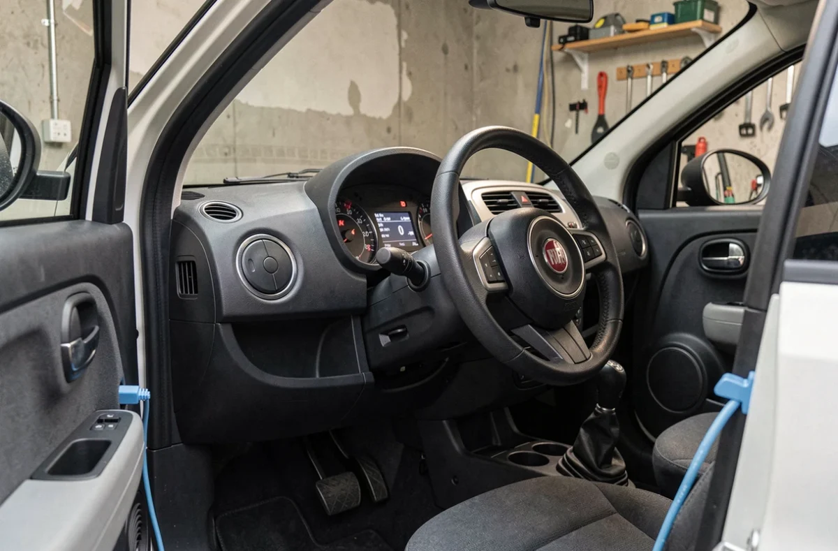 Intérieur minimaliste et tableau de bord d'une Fiat Topolino avec câble de recharge, illustrant les coûts et équipements inclus dans le budget mensuel